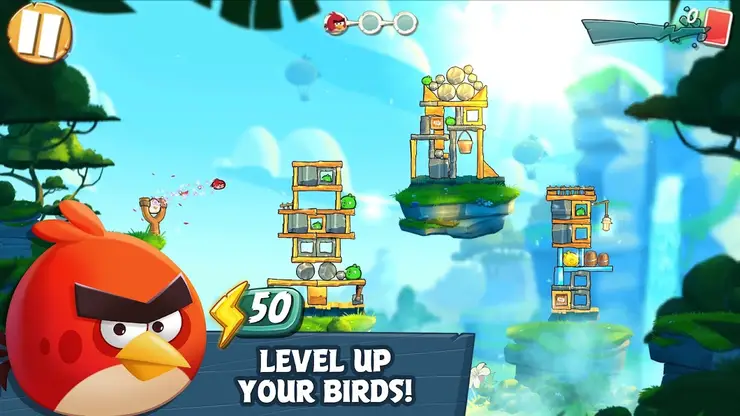 Csúzli a piros madárral, előtte lebegő szigeteken álló faszerkezetek, alul angol felirat – Level up your birds